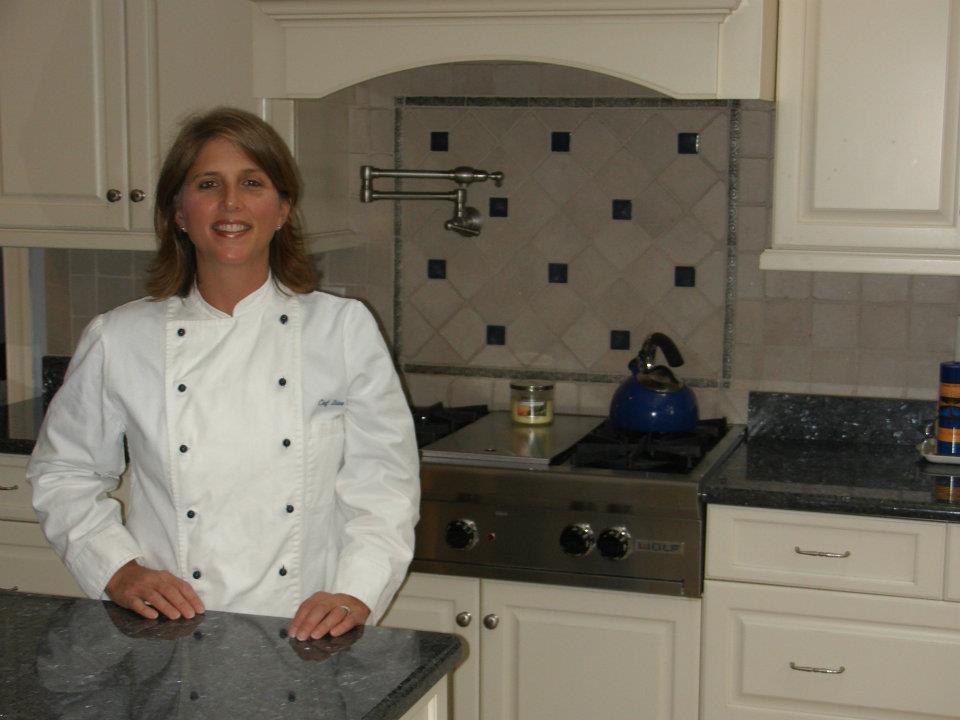 a chef in a white coat stands in a beautiful kitchen smiling at the camera